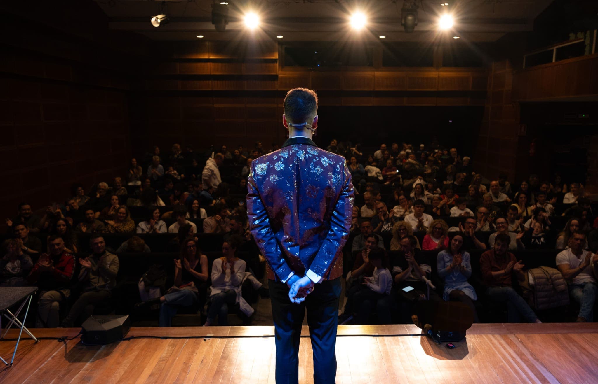 Alexander Main de espaldas sobre el escenario frente al público de un auditorio